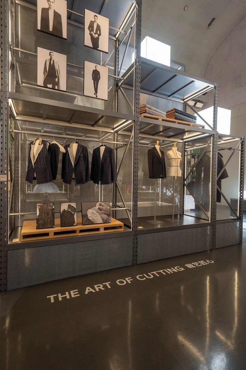 Sezione The Art of Cutting: giacche sartoriali scure e ritratti in bianco e nero su scaffalature metalliche – Max Mara The Max! al Long Museum, Shanghai, Cina, 2026 – allestimento espositivo
