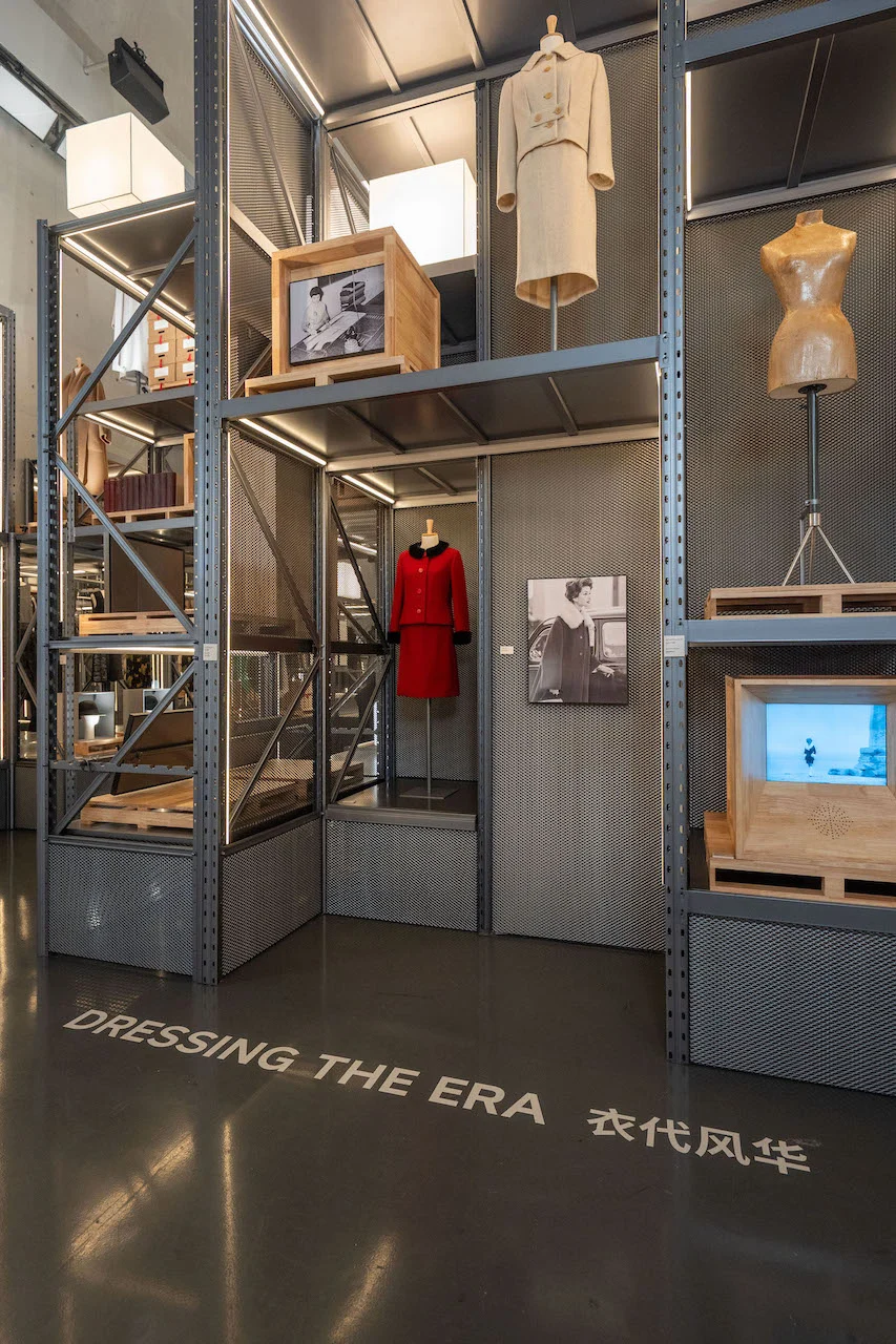 Sezione Dressing the Era: tailleur rosso, tailleur beige e un manichino da sarto su scaffalature metalliche con casse di legno – Max Mara The Max! al Long Museum, Shanghai, Cina, 2026 – allestimento espositivo