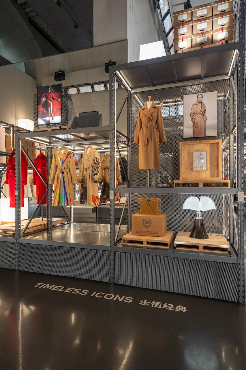 Scaffalatura metallica con cappotti cammello Max Mara, una lampada e casse di legno sopra la scritta a pavimento Timeless Icons – Max Mara The Max! al Long Museum, Shanghai, Cina, 2026 – allestimento espositivo