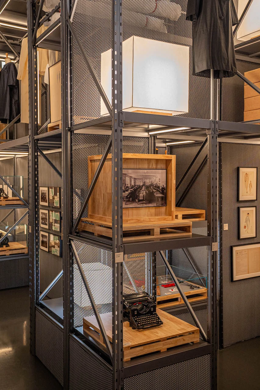 Alta torre di scaffali metallici con una lampada a cubo, una foto d'archivio incorniciata e una macchina da scrivere d'epoca su pallet – Max Mara The Max! al Long Museum, Shanghai, Cina, 2026 – allestimento espositivo