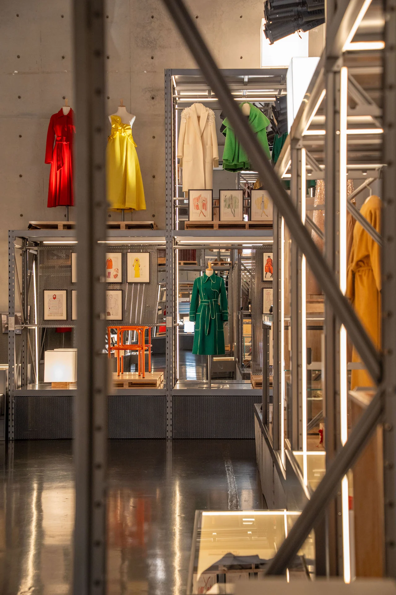 Vista attraverso un'impalcatura metallica di scaffali con capi rossi, gialli e verdi contro una parete di cemento – Max Mara The Max! al Long Museum, Shanghai, Cina, 2026 – allestimento espositivo
