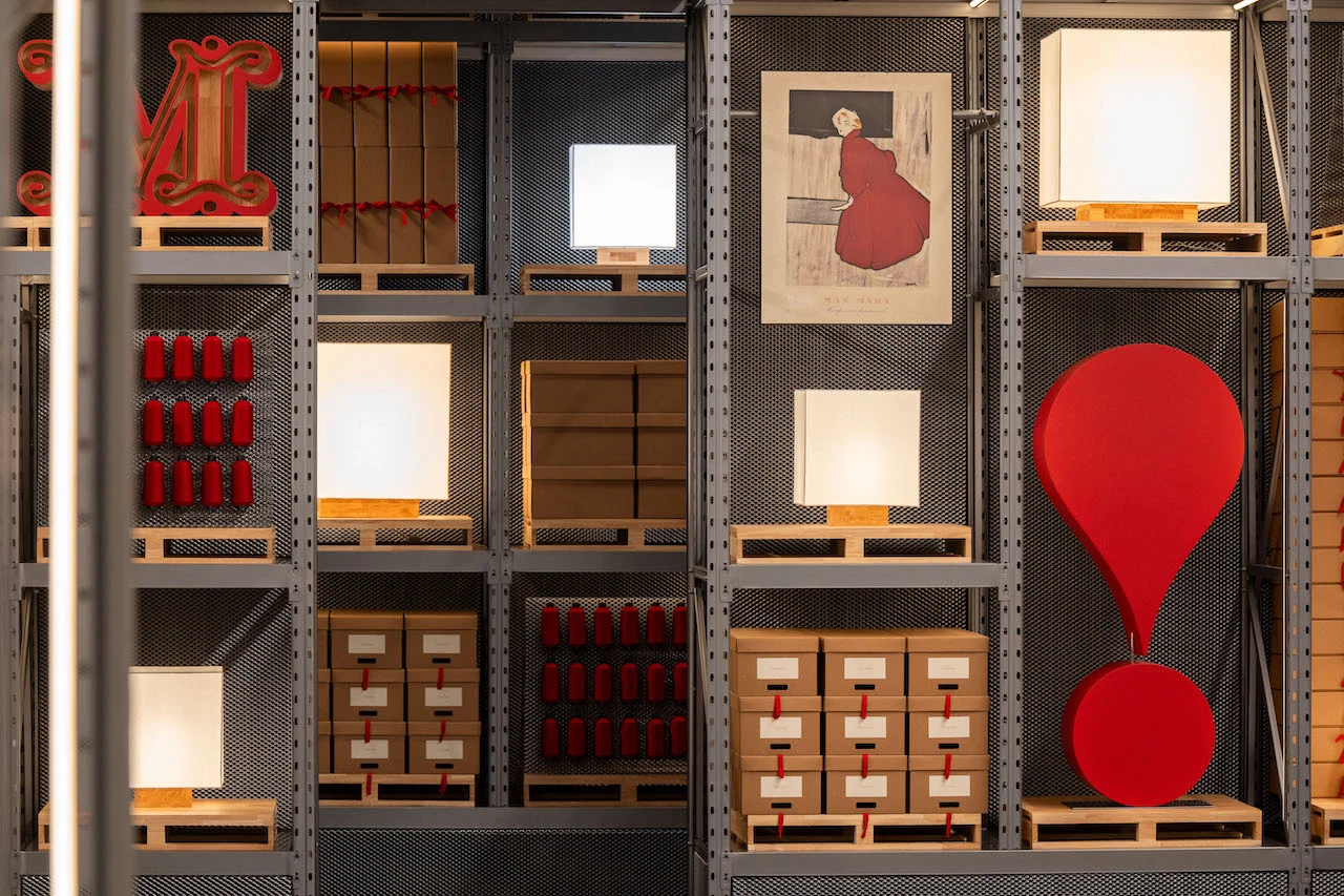 Parete di scaffalature metalliche con lampade a cubo, scatole d'archivio, rocchetti rossi e un grande punto esclamativo rosso – Max Mara The Max! al Long Museum, Shanghai, Cina, 2026 – allestimento espositivo