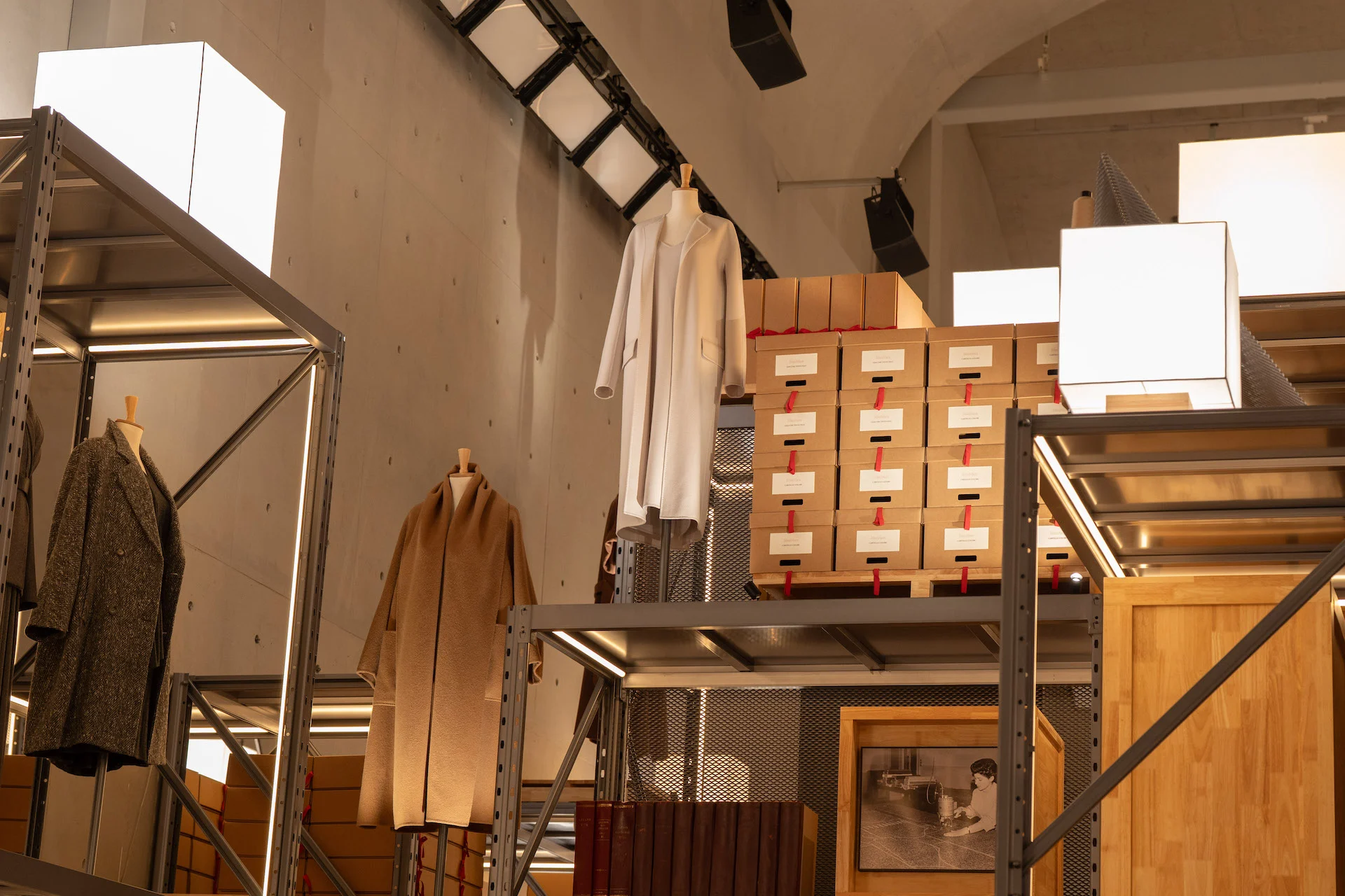 Livelli superiori dell'installazione di scaffali con cappotti, scatole d'archivio impilate e lampade a cubo sotto una volta di cemento – Max Mara The Max! al Long Museum, Shanghai, Cina, 2026 – allestimento espositivo