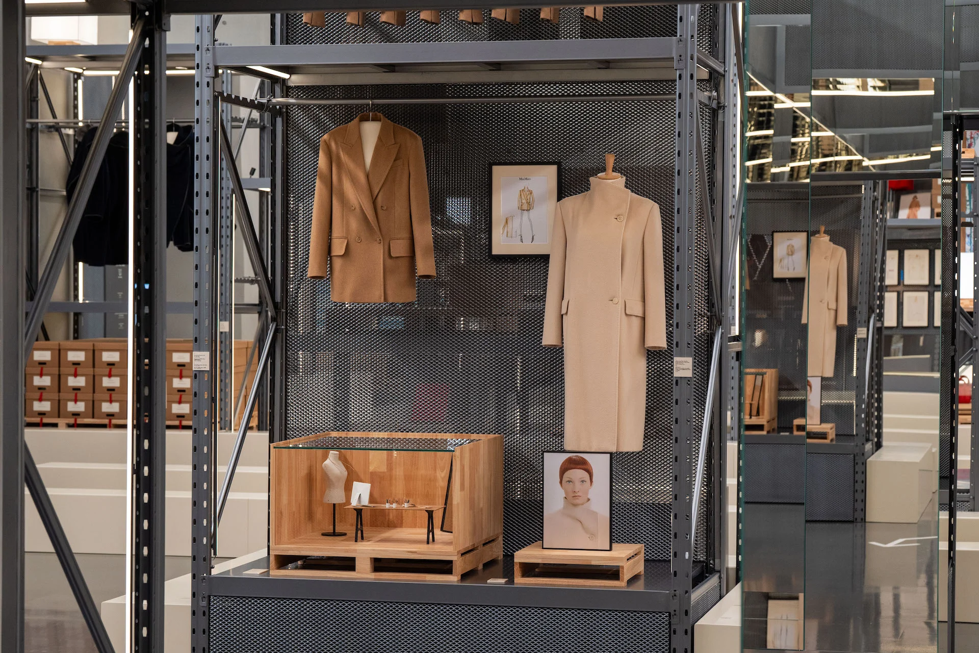 Due cappotti cammello e uno schizzo incorniciato su una scaffalatura in metallo forato, con una piccola vetrina in legno sotto – Max Mara The Max! al Long Museum, Shanghai, Cina, 2026 – allestimento espositivo