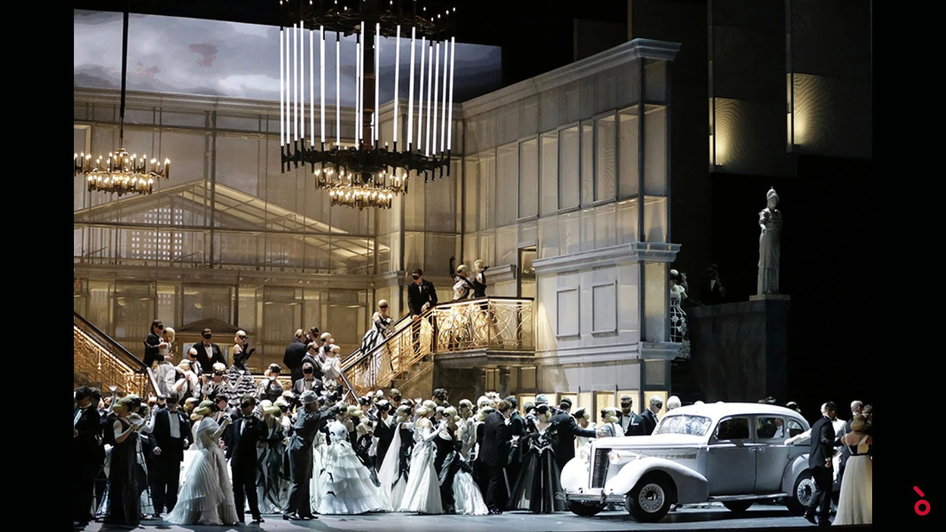 Scena del ballo con uno scalone, lampadari di cristallo, invitati in abito da sera e un'auto bianca d'epoca – Un Ballo in Maschera al Teatro Bolshoi, Mosca, Russia, 2018 – scenografia d'opera