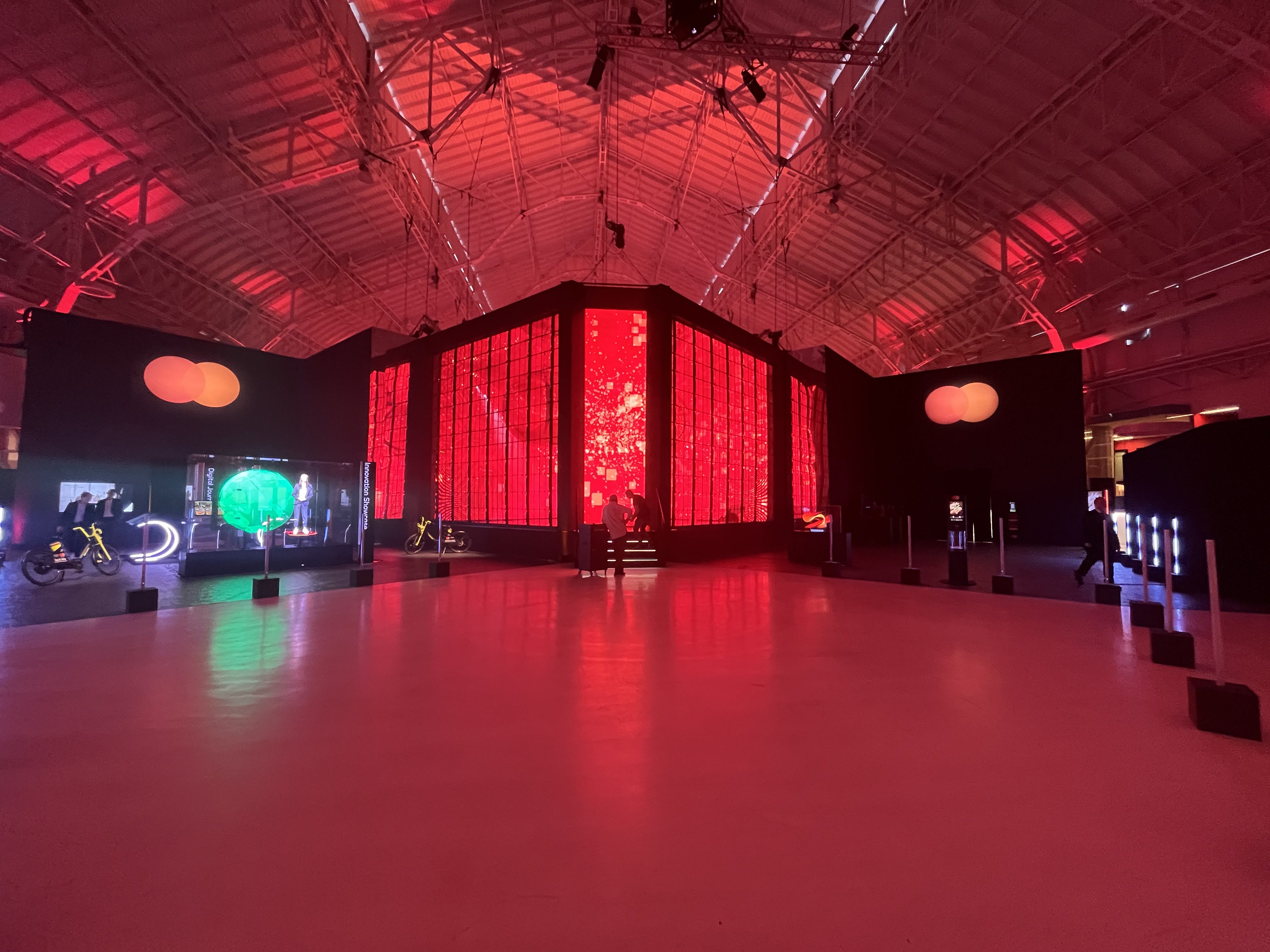 Capannone industriale immerso nella luce rossa, installazione di pareti LED al centro e postazioni interattive intorno – Mastercard Innovation Forum 2023, Milano, Italia – progettazione di eventi